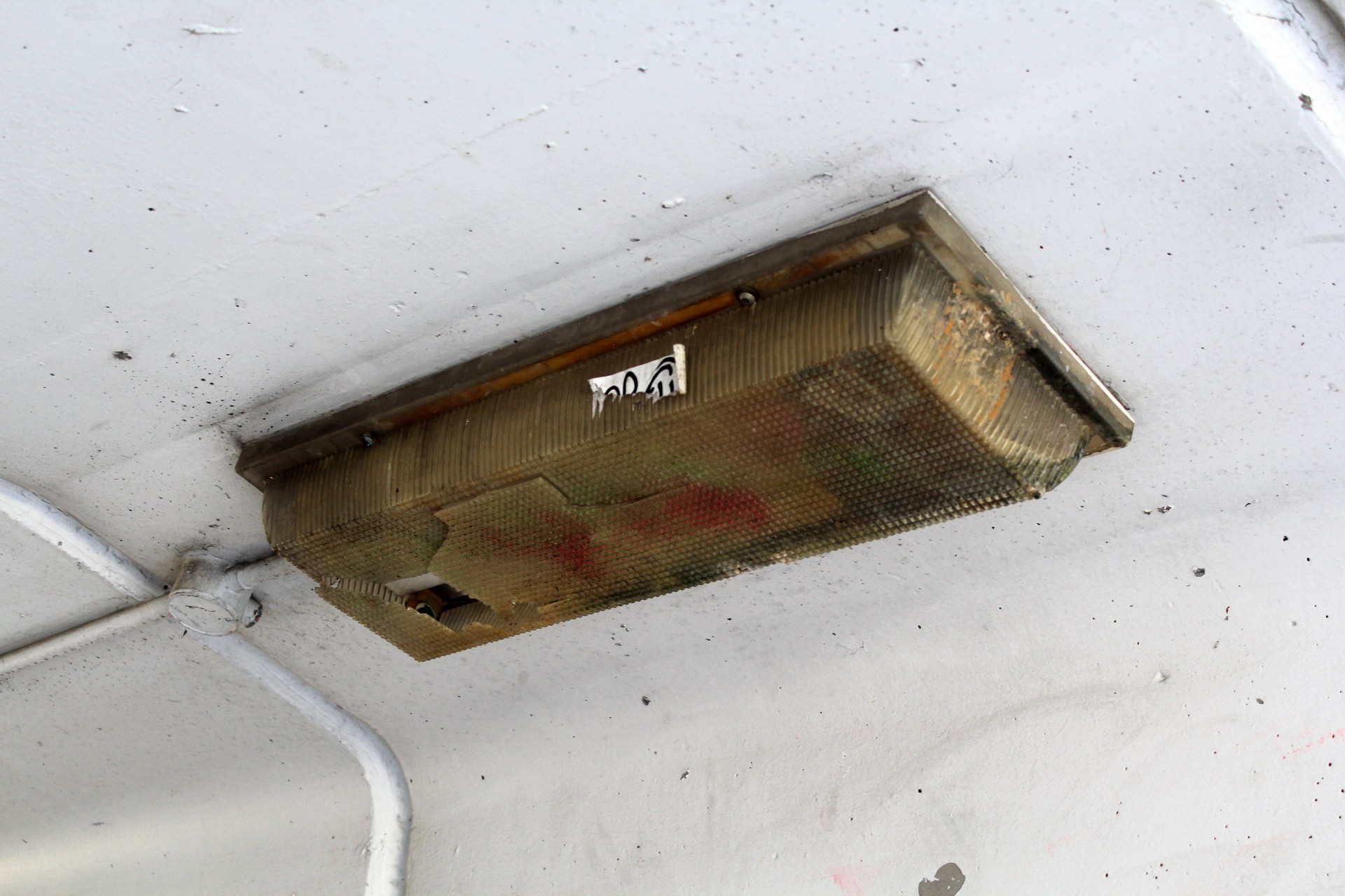 Damaged light fixture mounted on a white concrete ceiling emergency lithe, flick tests, broken emls, led indicator, fire exit escape, fire exit door, emergency light exit